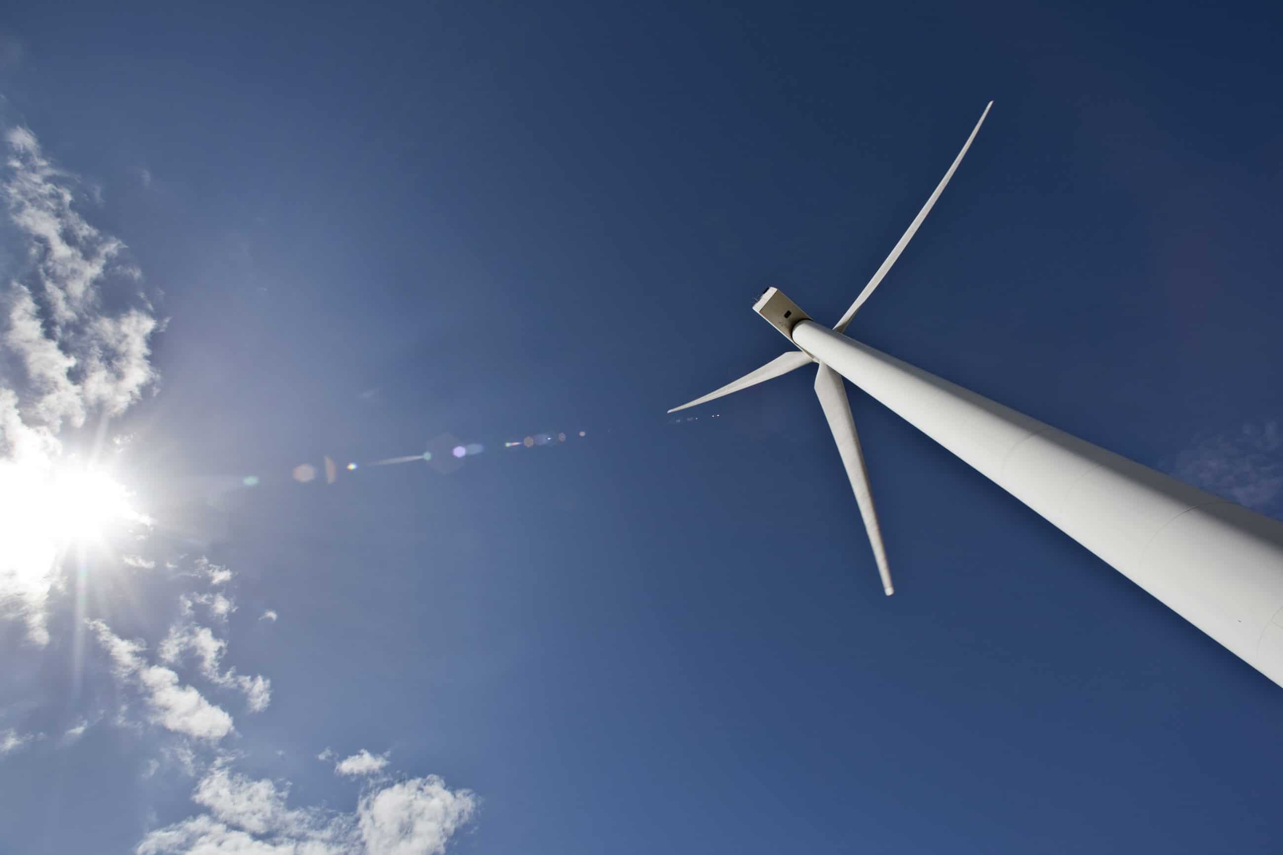 wind turbine towering over the viewer with blue skies and the sun shining in the background