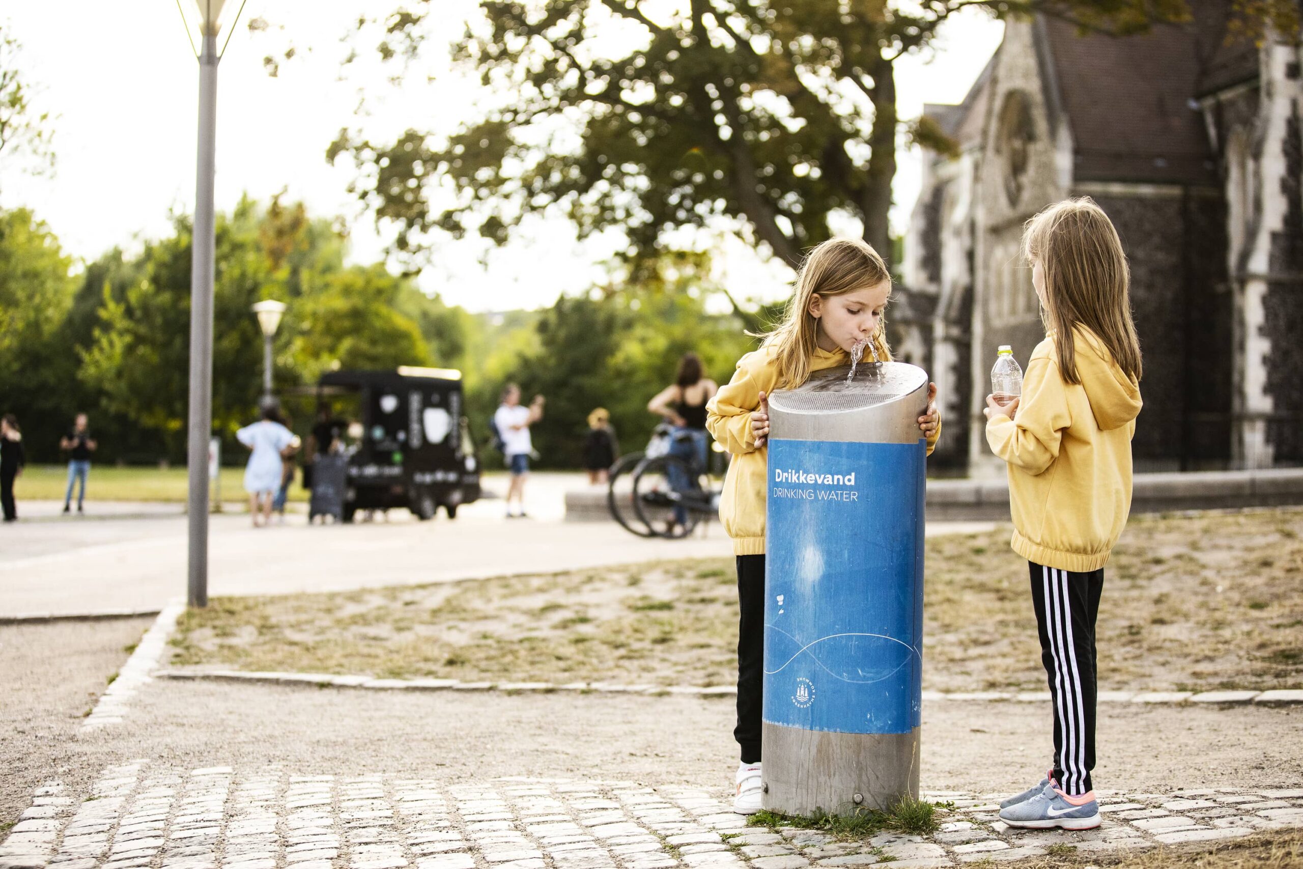 Two girls drinking water from a water station in a park
